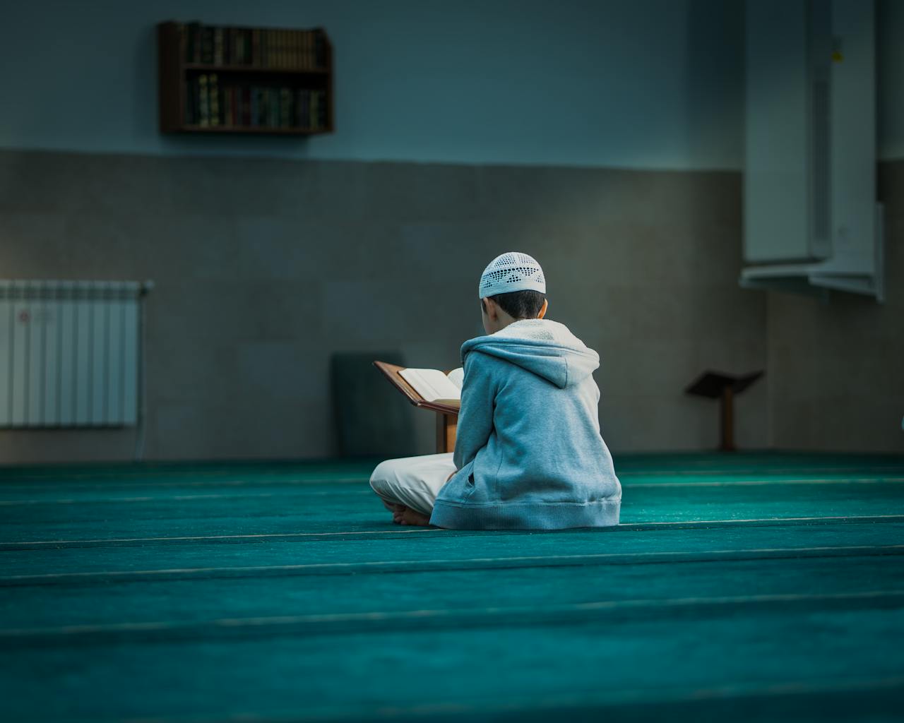 hero-img-01 A boy in a mosque in Algeria reading religious texts, emphasizing peace and devotion.