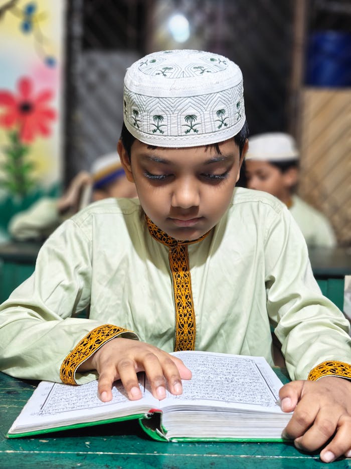 gallery-2 A concentrated young boy wearing a traditional cap reads a religious book at a table.